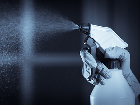 A black and white photo of a gloved hand spraying a spray bottle.