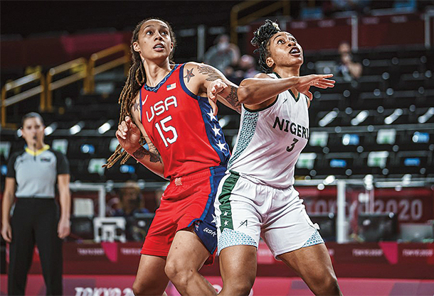Two women playing basketball await the ball as it falls.