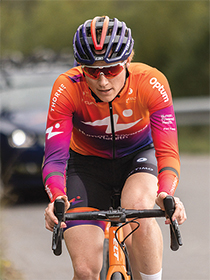 Woman biking facing forward, wearing pink purple and orange long sleeve and black helmet.