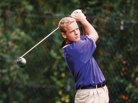 Luke Donald holds his golf club up after a large swing, he watches his golf ball fly.