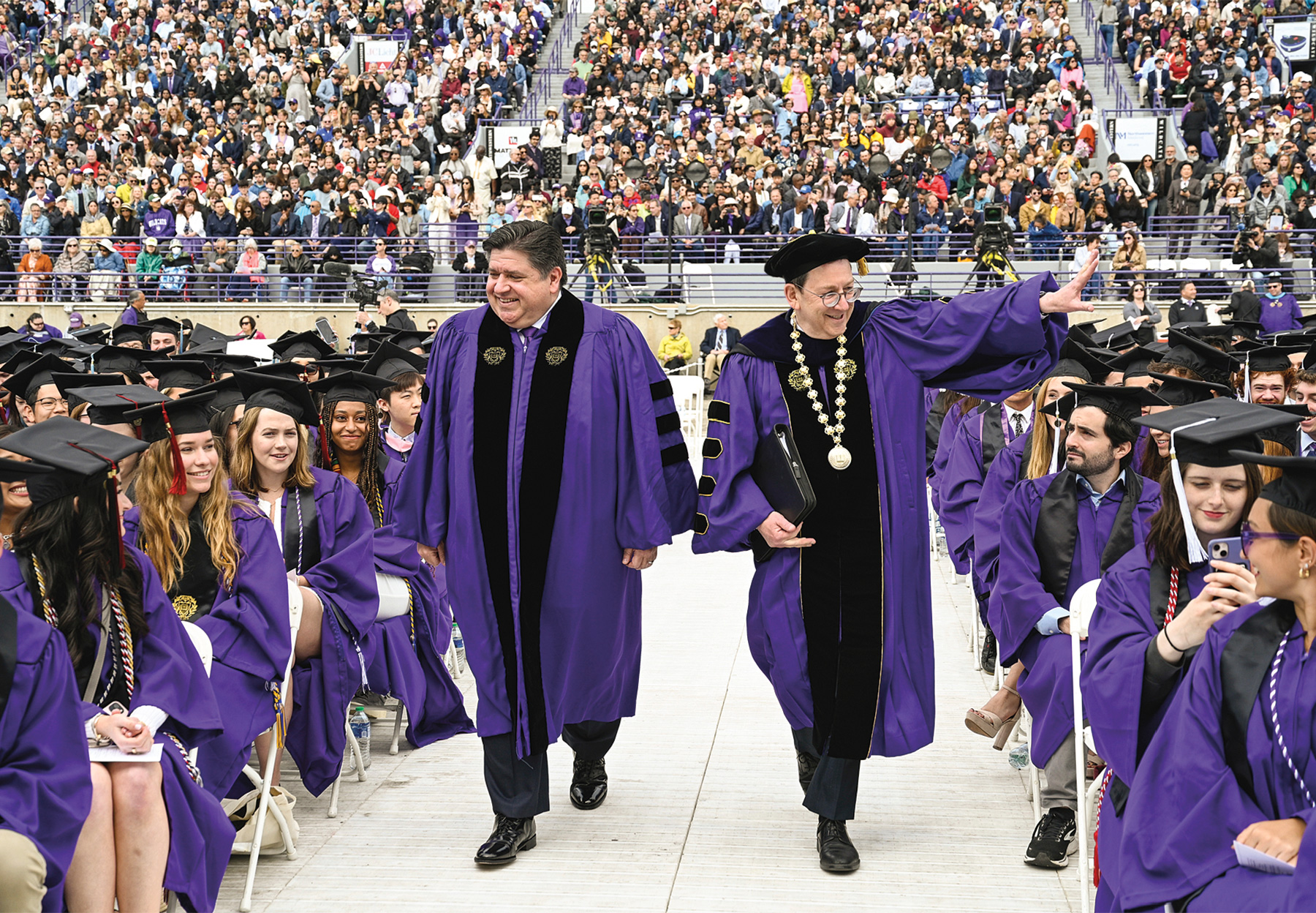 Governor Pritzker walks with President Schill down rows of graduates on commencement day.