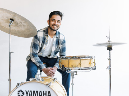 Darsan Swaroop Bellie poses with a Yamaha drum set in front of a white background.