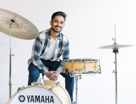Darsan Swaroop Bellie poses with a Yamaha drum set in front of a white background.