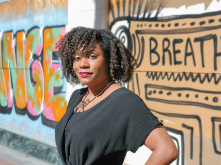 Kyra Kyles stands in front of a mural with her hand on her hip.