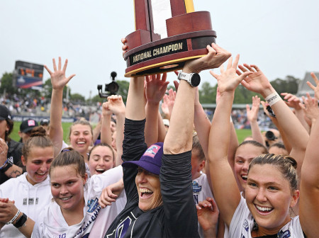 The women's lacrosse team cheers and holds up their National Champions trophy.