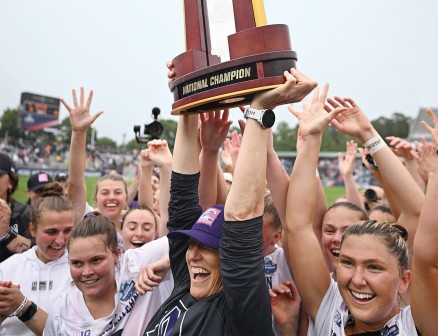 The women's lacrosse team cheers and holds up their National Champions trophy.