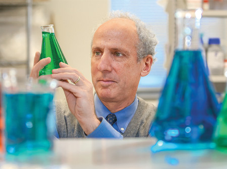 Robert Kalb examines a beaker with green fluid inside.