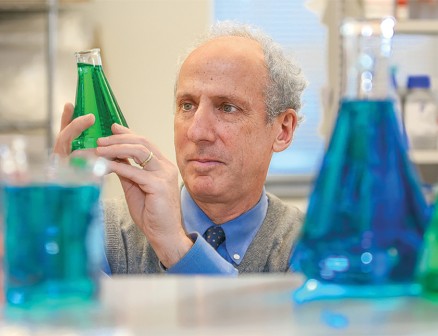 Robert Kalb examines a beaker with green fluid inside.