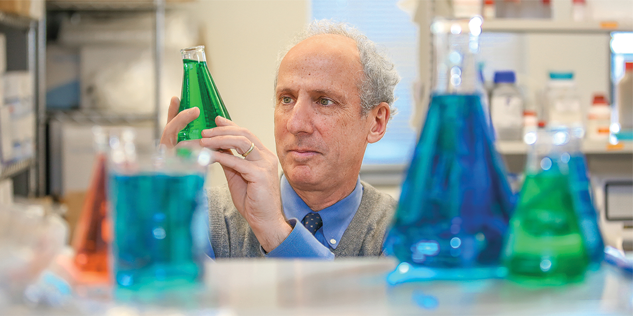 Robert Kalb examines a beaker with green fluid inside.