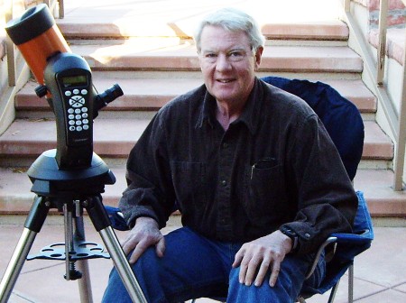Tim Hunter sits in a camping chair smiling, in front of a large telescope.