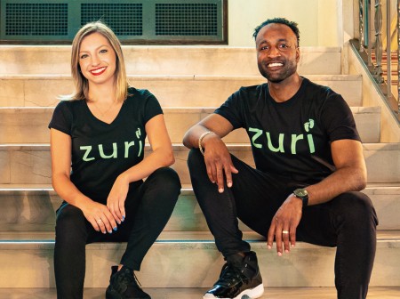 Giuliana Zaccardelli and Blair Matthews sit on steps next to each other smiling for a photo, both are wearing "Zuri" shirts.