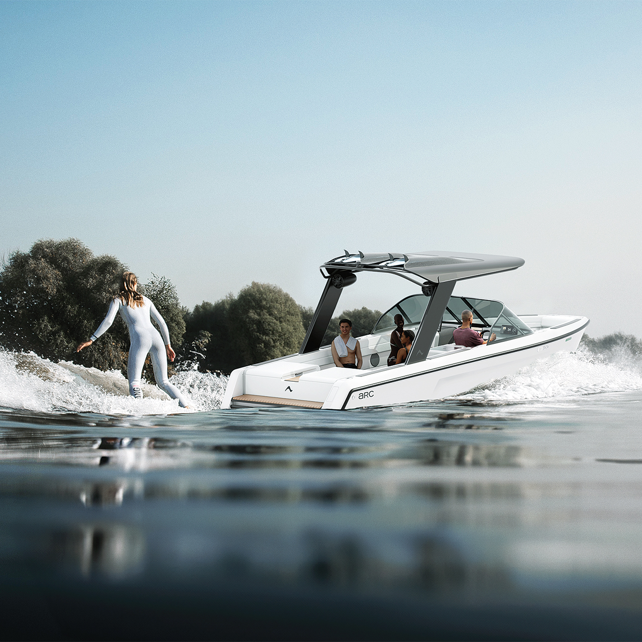 Three people sit aboard the Arc Sport EV boat. A woman wake boarder in a silver suit rides on a board behind the boat. Her back is to the viewer. There are green trees in the background.