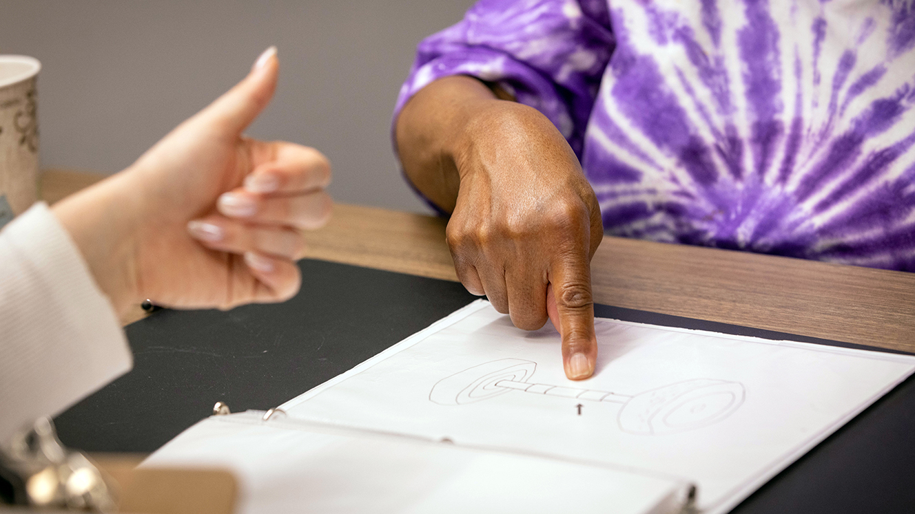 Yvonne Gregwor, wearing a purple tie-dyed t-shirt, points to a page in a binder while a researcher gives a thumbs-up.