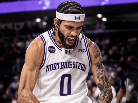 Basketball player Boo Buie, in a white Northwestern jersey with the number 0, flexes during a game.