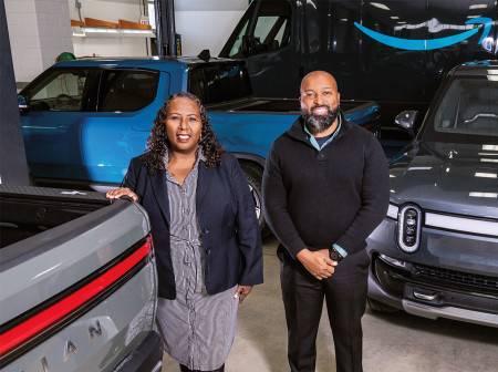 Cheryl Freeman-Smith and Brandon Nichols stand beside several Rivian electric vehicles.