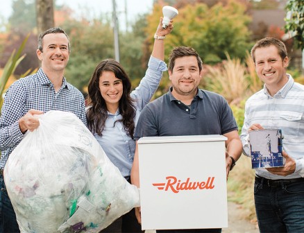 Ridwell founders Ryan Metzger, Aliya Marder, Justin Gough and David Dawson stand outside holding a variety of recyclable items and a Ridwell recycling container.