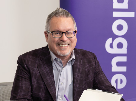 A man wearing glasses and a suit smiles while signing a book.