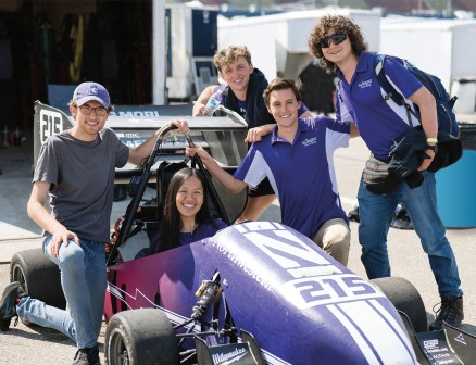 Team smiles around a Northwestern branded race car