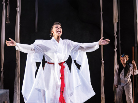 A performer in a white costume with a red belt opens her arms to the audience.