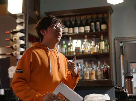 Shane Chung holds a collection of papers while gesturing with his left hand while standing inside a bar.