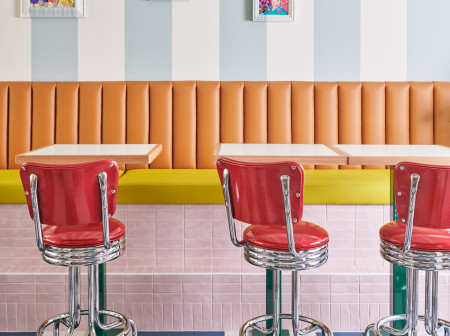 A photo of Hilda and Jesse’s dining room, with red diner stools and a brightly colored interior featuring framed artwork and a blue-and-white striped wall.