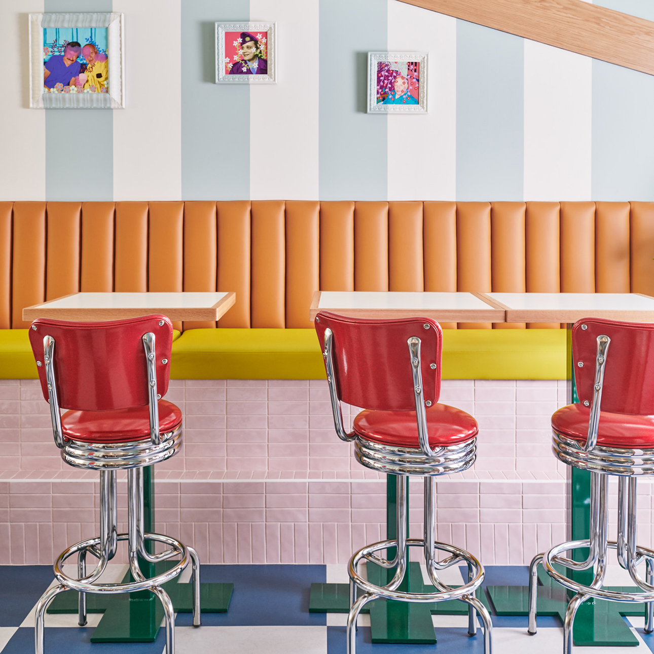 A photo of Hilda and Jesse’s dining room, with red diner stools and a brightly colored interior featuring framed artwork and a blue-and-white striped wall.