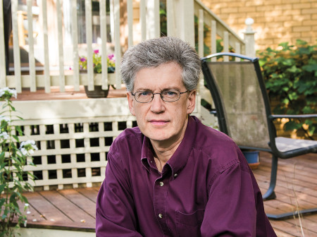 Kevin Boyle sits at a table outside, wearing a purple collared shirt. 