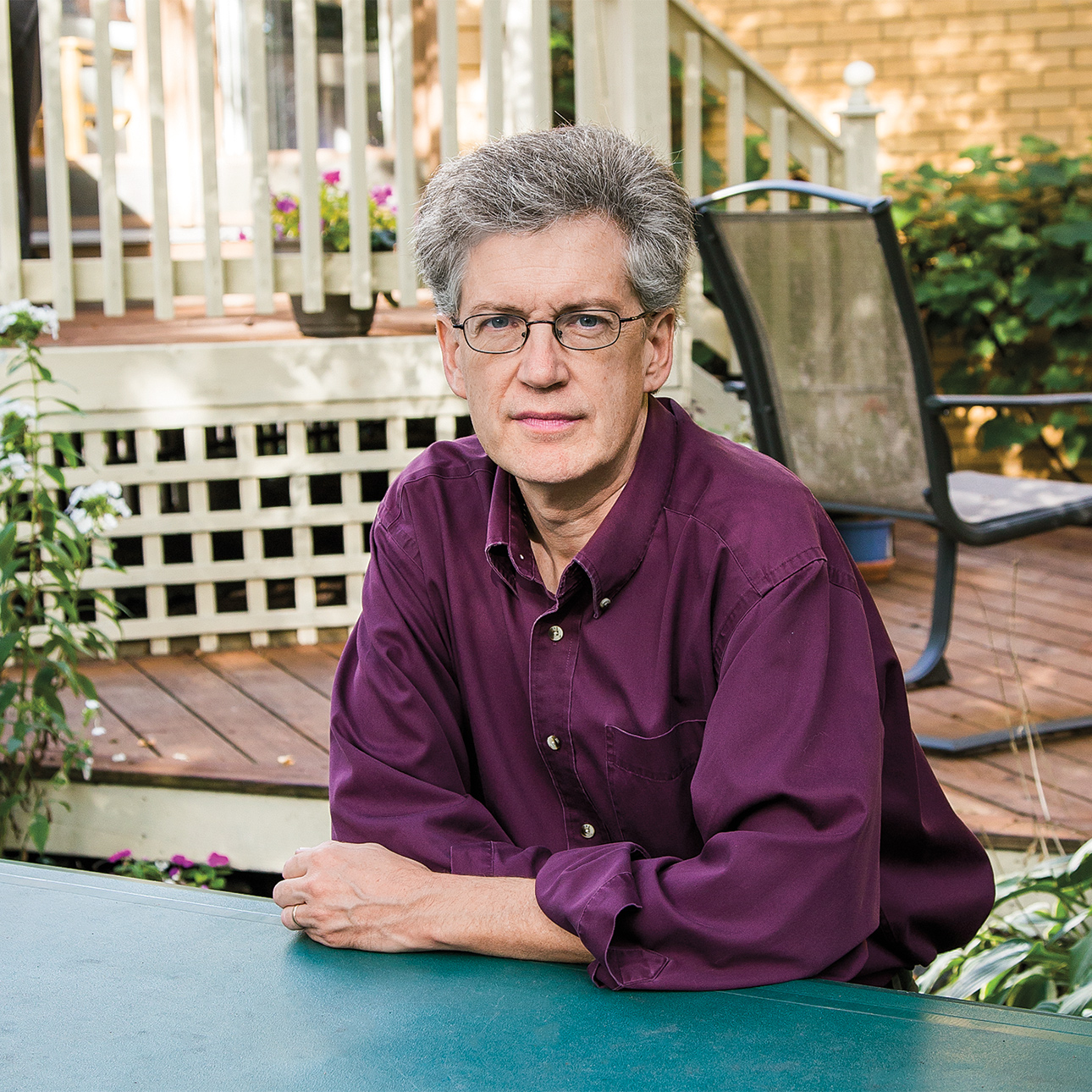 Kevin Boyle sits at a table outside, wearing a purple collared shirt. 
