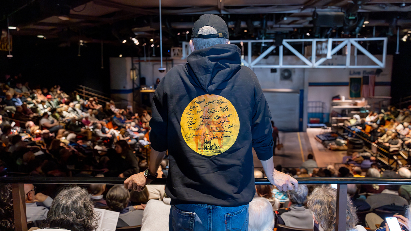 Henry Godinez stands with his back to the camera, overlooking the audience in the Barber Theater.  