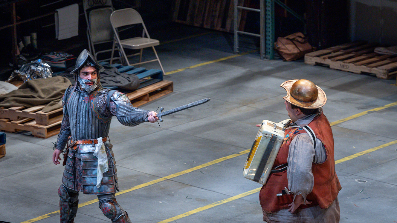 Don Quixote points a sword at the Barber, who wears a wash basic as a hat and is holding an accordion. 