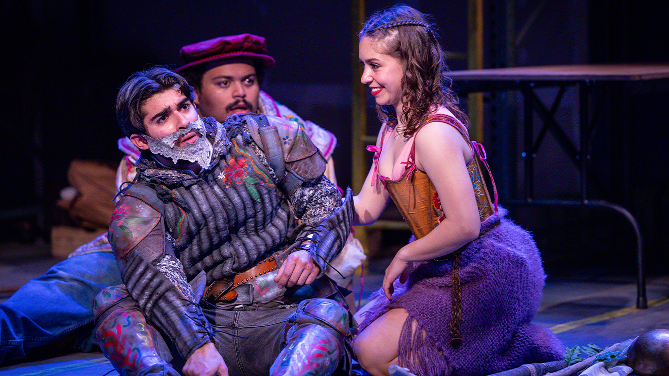 Don Quixote, Sancho and Aldonza sit on the ground together. Quixote and Sancho appear shocked. Aldonza smiles. 