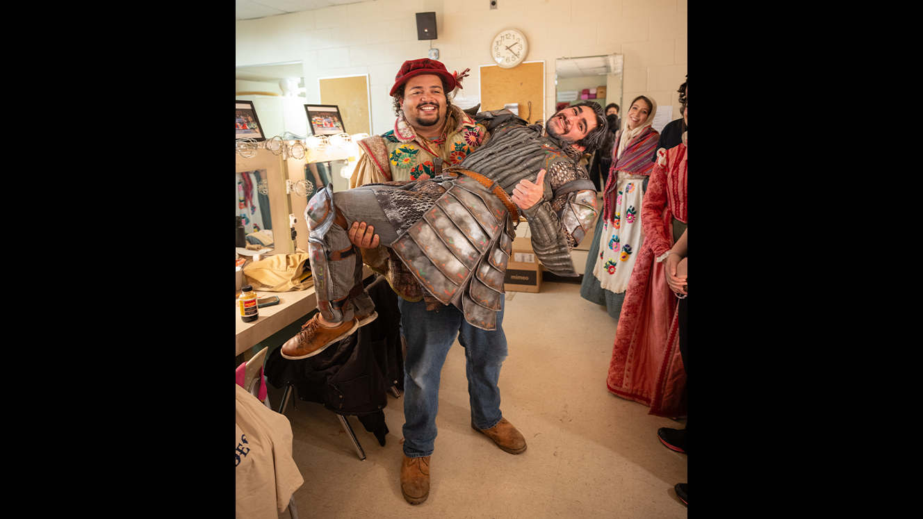 Sancho carries Quixote in his arms in one of the dressing rooms. 