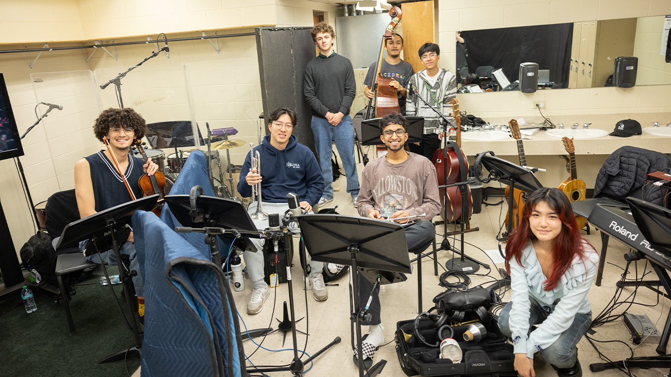 A group of musicians pose for a picture with their instruments in a dressing room. 