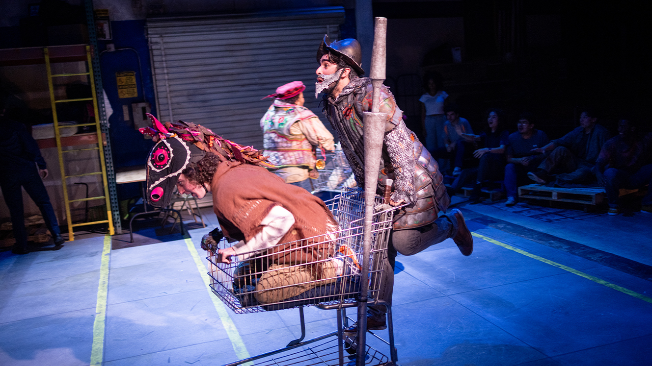 Don Quixote pushes a grocery cart on stage. Inside the cart is an actor wearing a horse head. 
