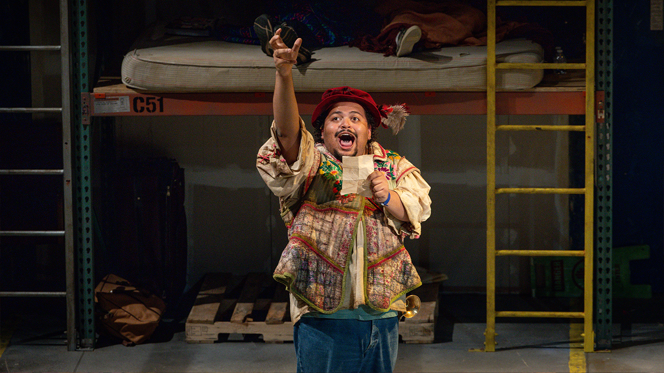 Sancho sings on stage. He holds his right arm up high while his left hand holds a piece of paper. 