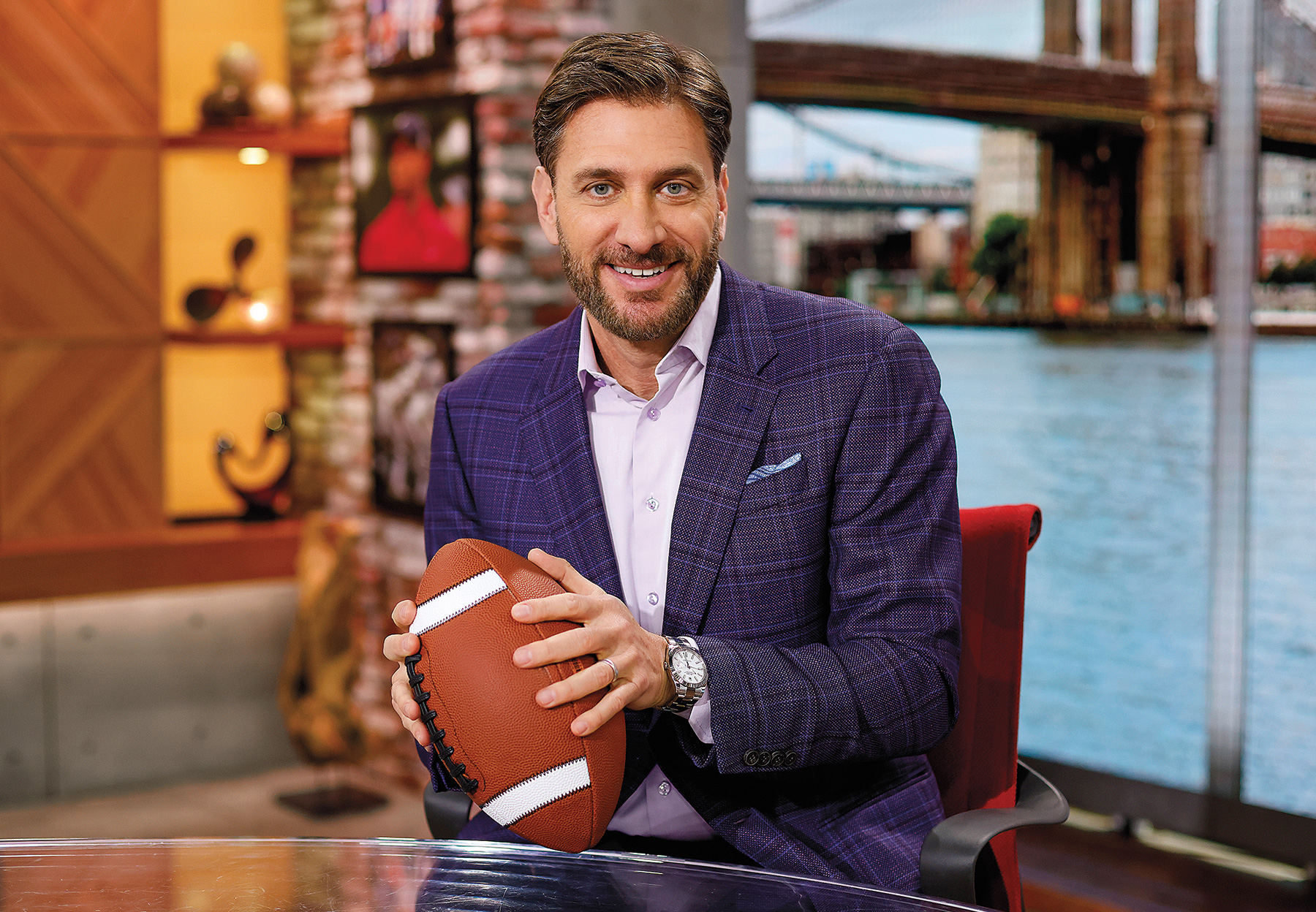 Michael D. Greenberg holds a football and looks at the camera while sitting in a chair.