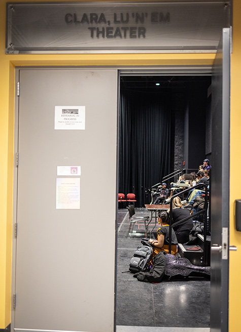 A doorway opens into a black box theater, where students are seated. Above the doorway is a sign reading Clara, Lu’n’em Theater.