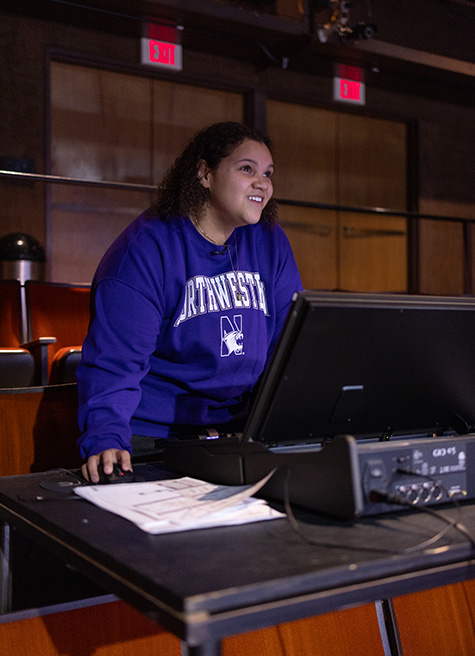 Sierra Walker wears a purple Northwestern sweatshirt while operating her lightboard from the seating area in the Barber Theater.