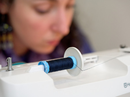 A white machine holds a spool of thread. 