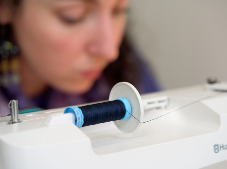 A white machine holds a spool of thread. 