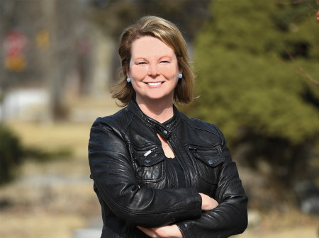 Julia Starzyk Kersey, wearing a black leather jacket, stands with her arms folded across her chest.