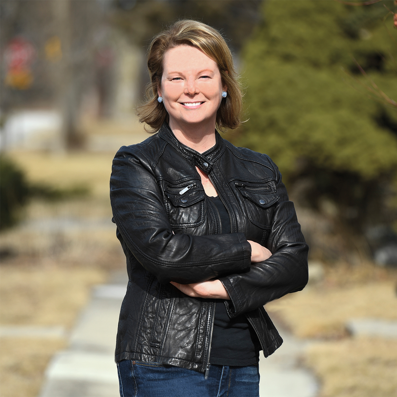 Julia Starzyk Kersey, wearing a black leather jacket, stands with her arms folded across her chest.