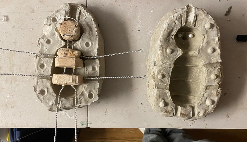 A bug-shaped clay mold with wire pieces sticking out, sitting on a table.