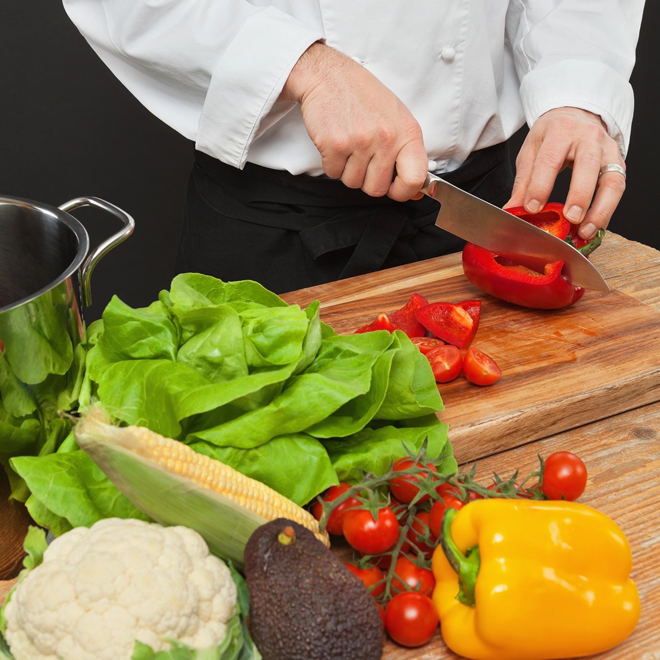 A chef slices vegetables on a wooden cutting board.