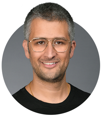 Adam Waytz is smiling at the camera. He is wearing a black shirt and glasses.