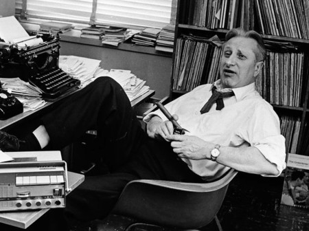 A grayscale image of Studs Terkel leaning back in an office chair surrounded by books and a typewriter.