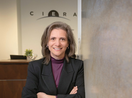 With her arms folded, professor Vicky Kalogera leans against a wall with the CIERA logo in the background.