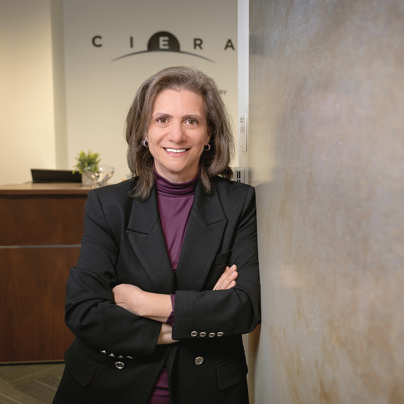 With her arms folded, professor Vicky Kalogera leans against a wall with the CIERA logo in the background.