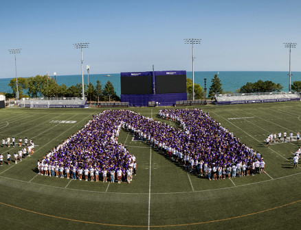 An aerial view of students from the Class of 2028 on a football field, where the students are arranged to form a giant purple N as well as the number 2028.