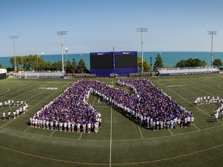 An aerial view of students from the Class of 2028 on a football field, where the students are arranged to form a giant purple N as well as the number 2028.